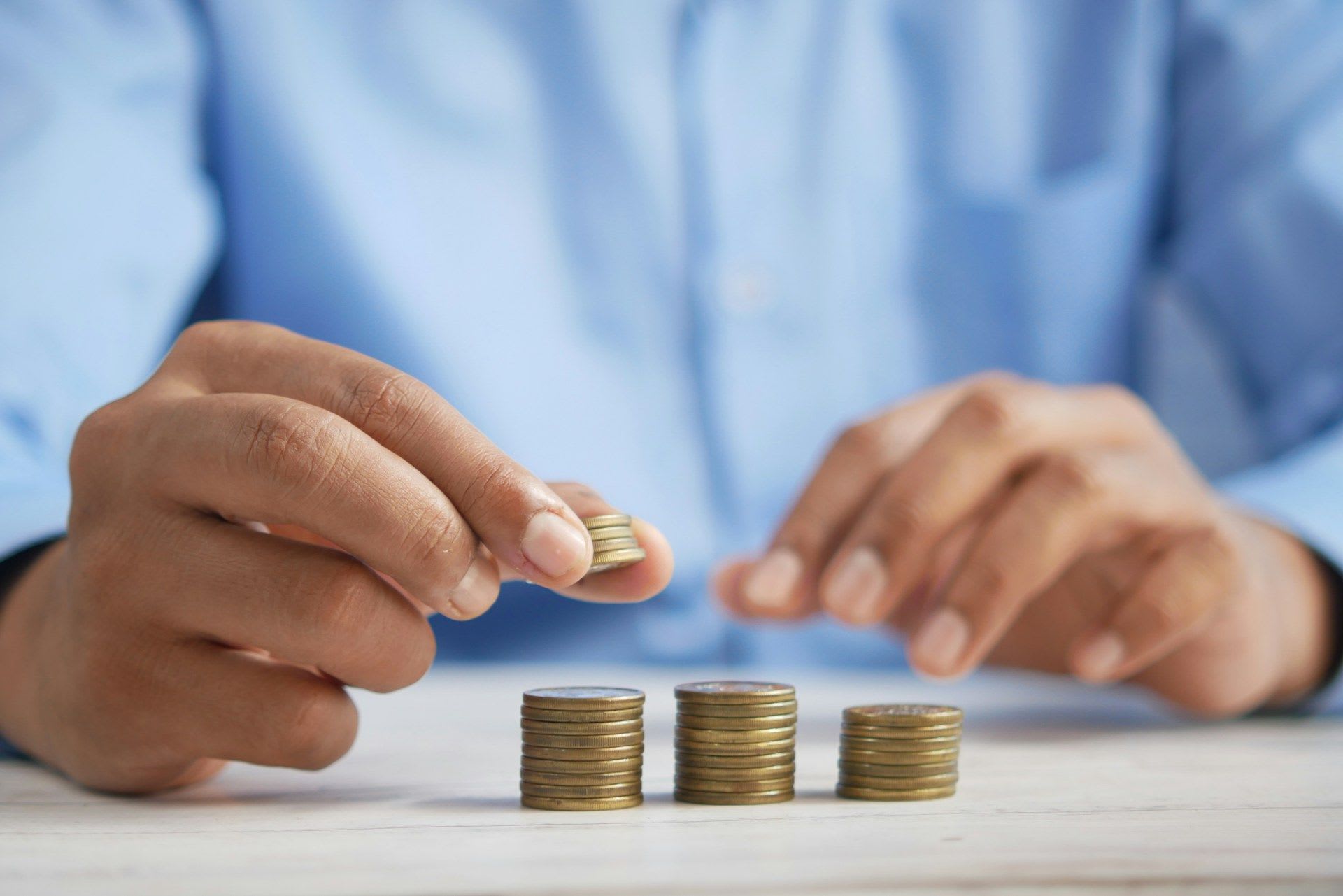 Three stacks of coins with a hand adding coins.