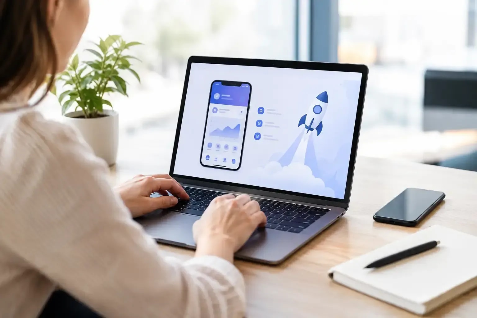 A woman working on a laptop with a mobile app mockup on the screen.