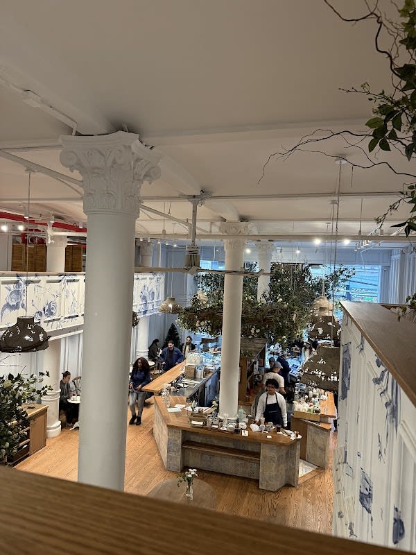 Overhead view of an elegant cafe interior featuring ornate white columns, blue and white patterned walls, wooden countertop bar, hanging greenery, and staff serving customers
