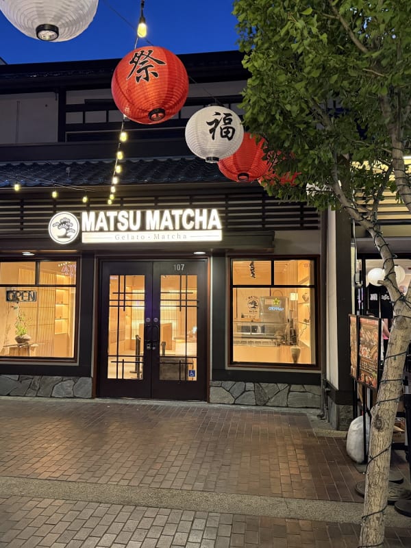 Exterior of Matsu Matcha gelato and matcha shop at night, storefront lit with warm lighting, red and white Japanese lanterns hanging above entrance