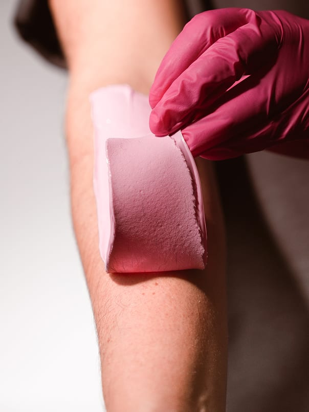 Esthetician removing Plumeria hard wax strip from client's leg in one clean pull