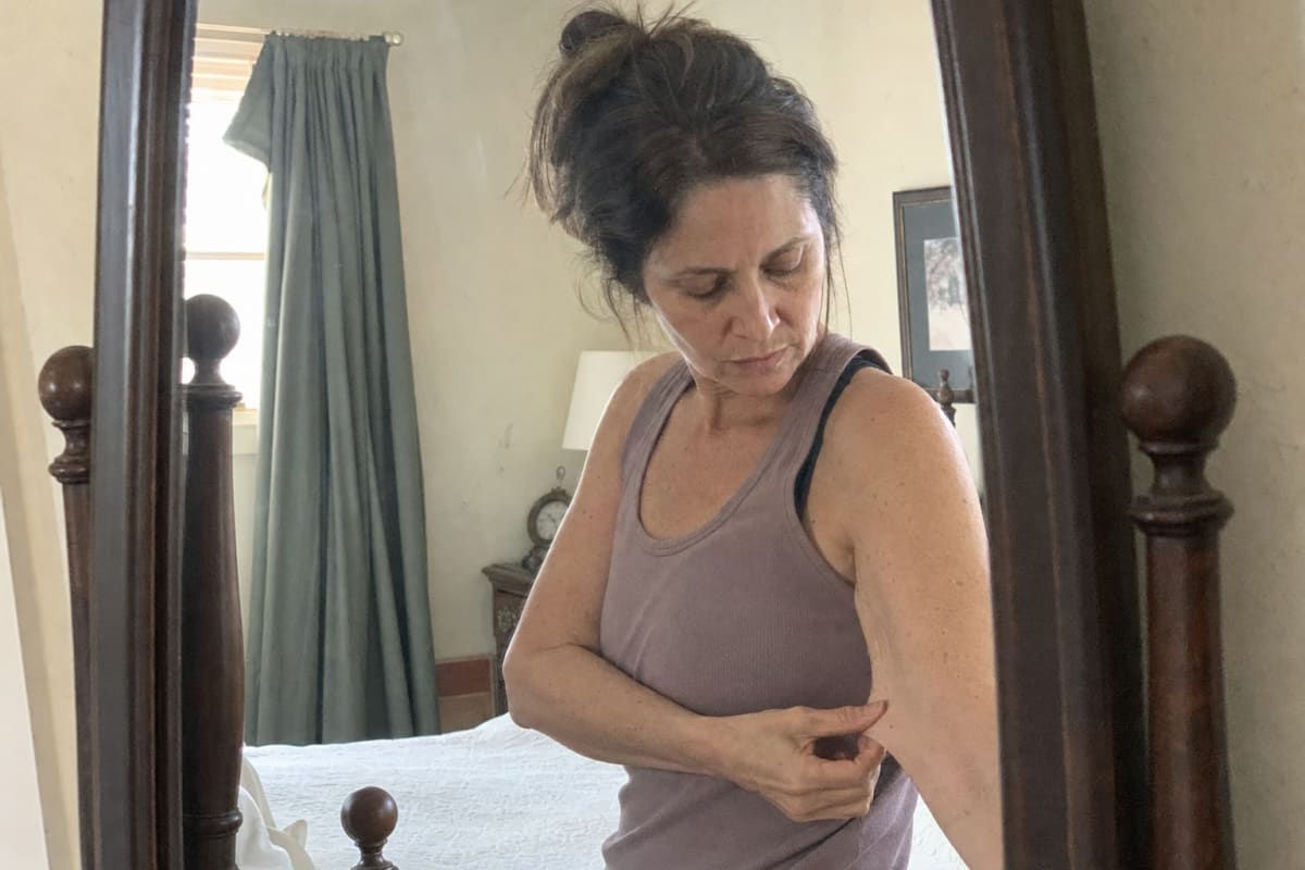 A woman noticing her thinner, softer arm in the mirror