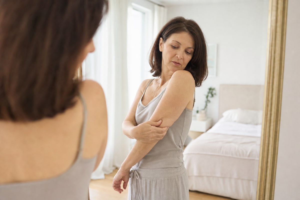 A woman noticing her thinner, softer arm in the mirror