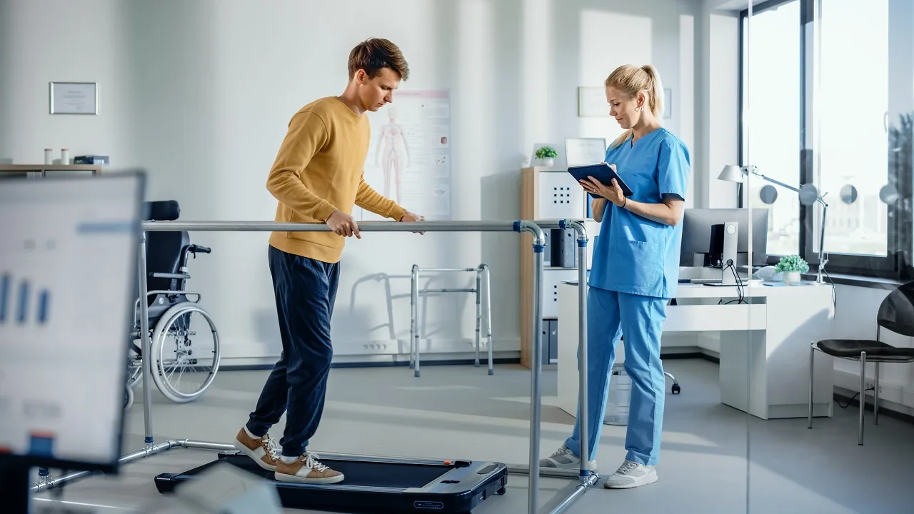 Physical therapist guiding a patient through parallel bars rehabilitation at a PT of The City clinic in Manhattan