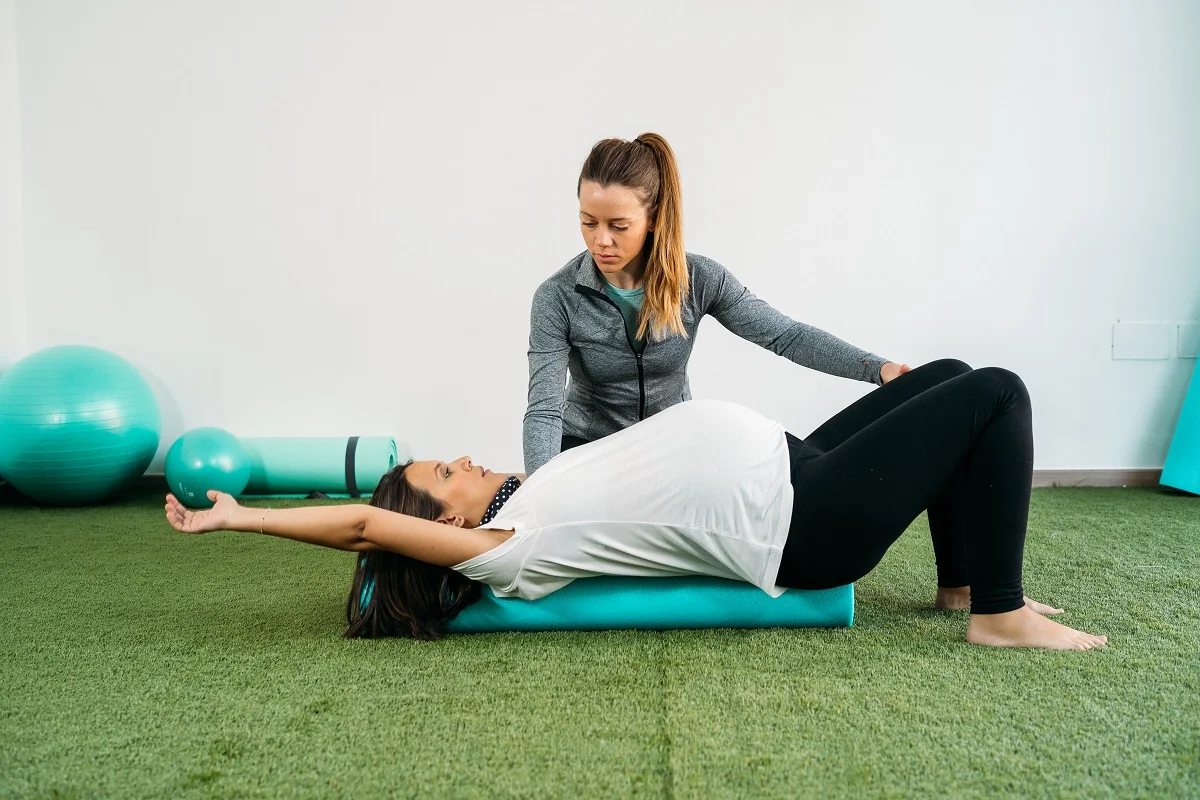 Female physical therapist guiding a pregnant patient through a floor exercise