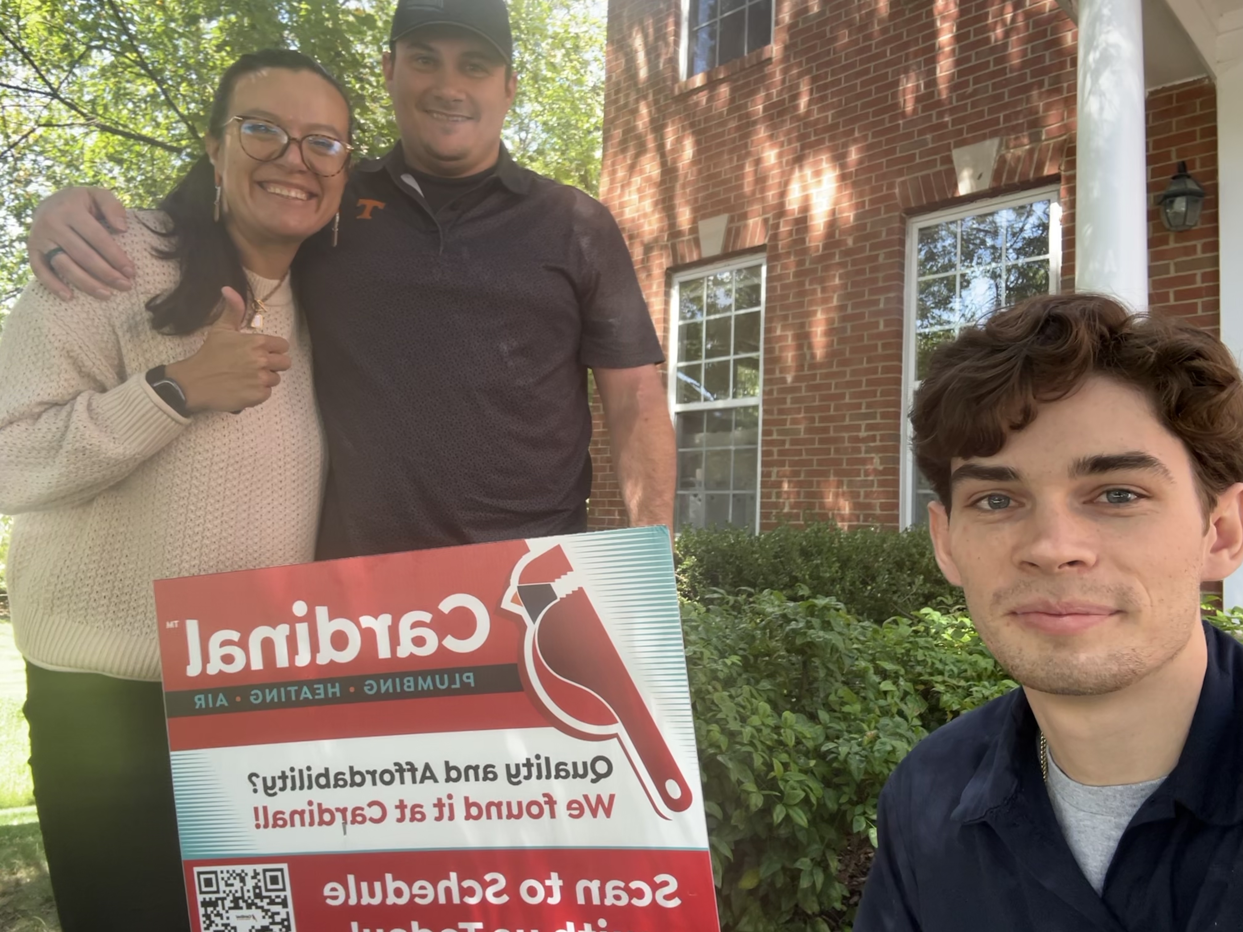 Smiling homeowners and our team showcase a Cardinal Plumbing Heating & Air Inc sign, highlighting friendly, reliable service at your home.