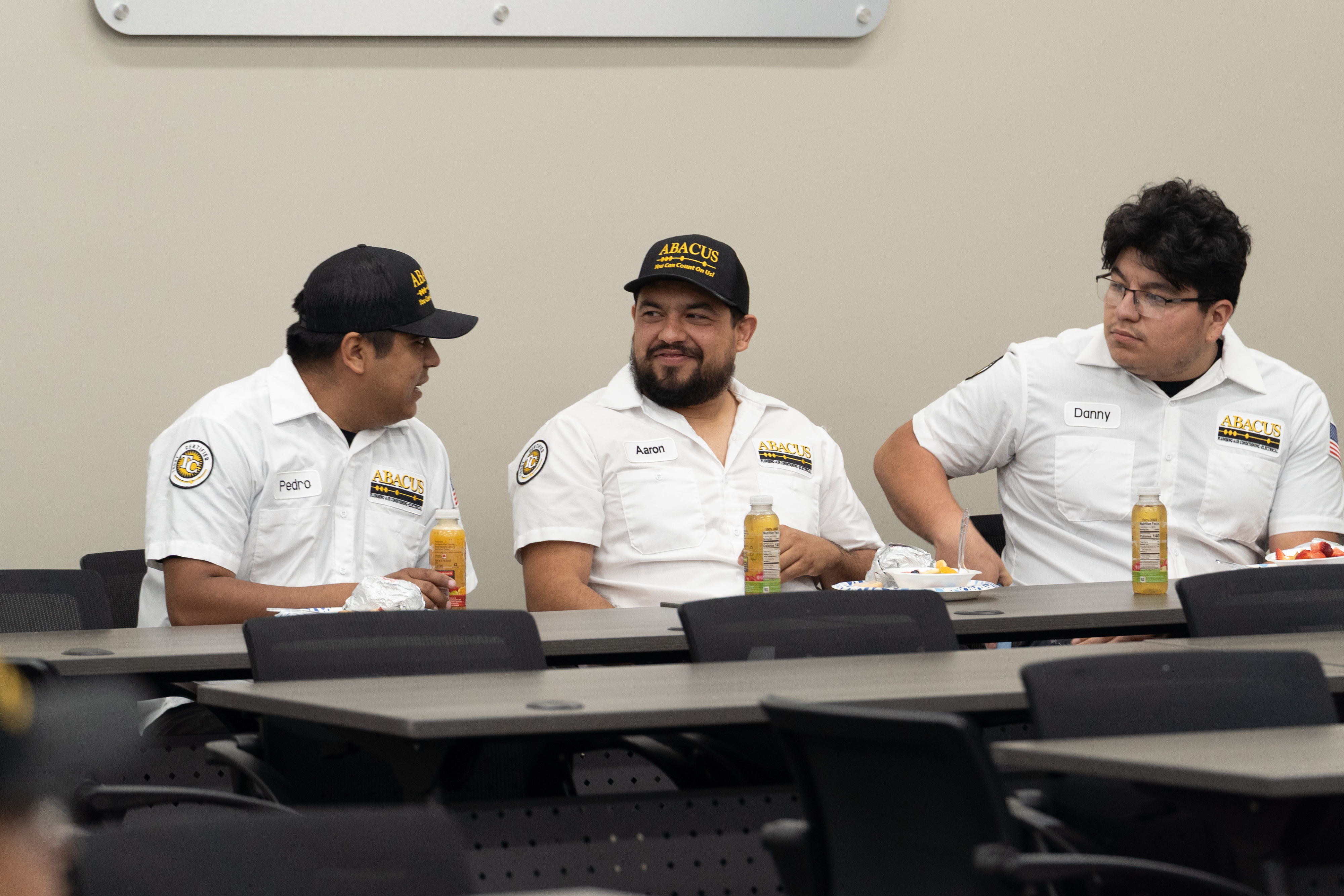 Friendly technicians from Abacus Plumbing, Air Conditioning, & Electrical showcase a professional, approachable team atmosphere during staff training and lunch.