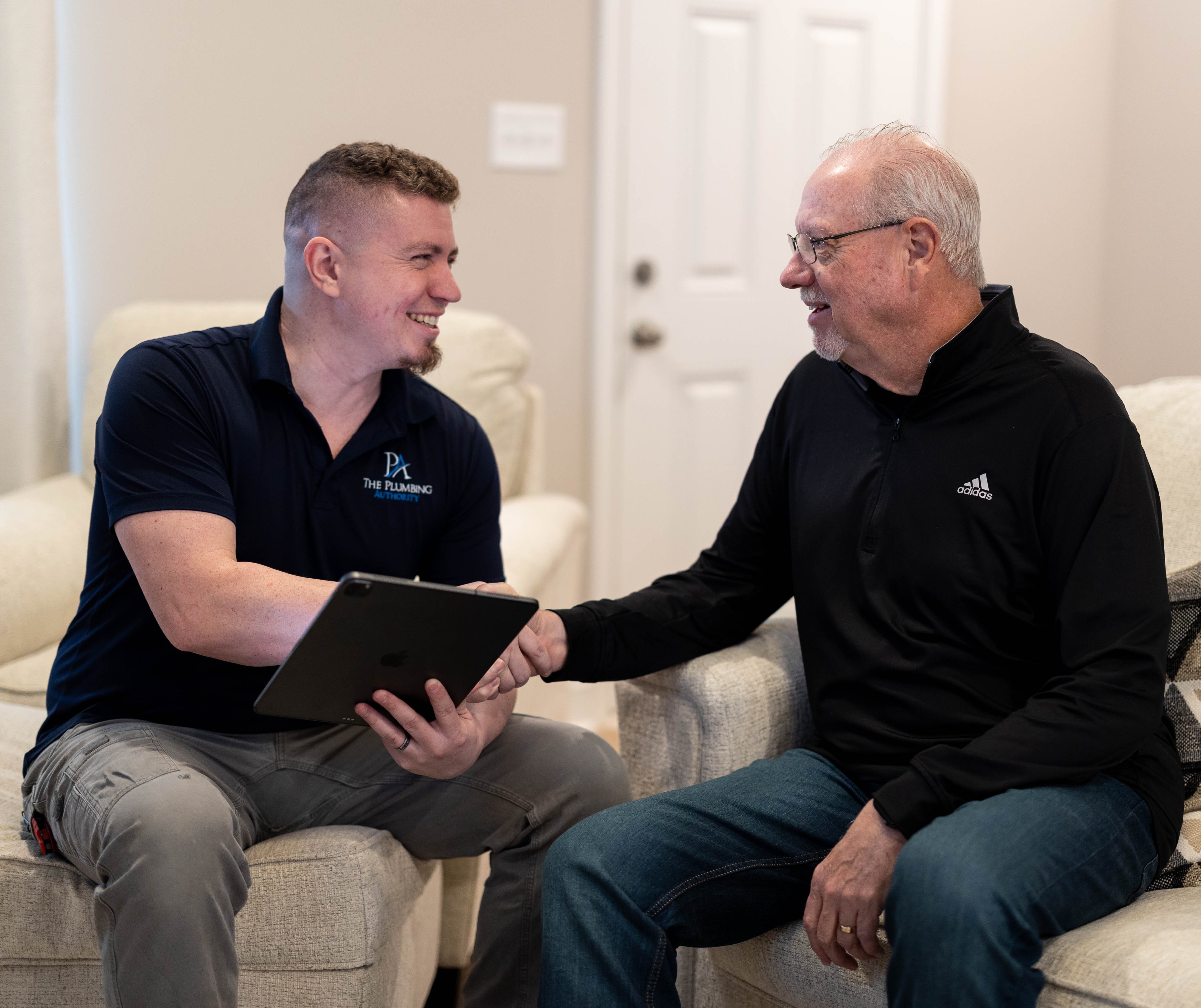 A friendly technician from The Plumbing Authority meets a homeowner in their living room, delivering professional service and clear guidance.