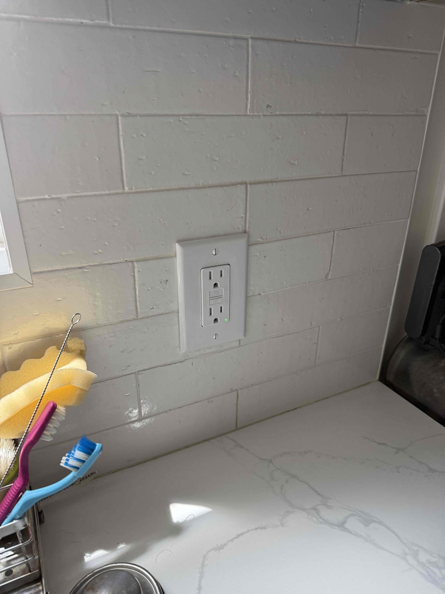 Powell Electric installed a tidy GFCI outlet that enhances kitchen safety and blends seamlessly with the clean tile backsplash.