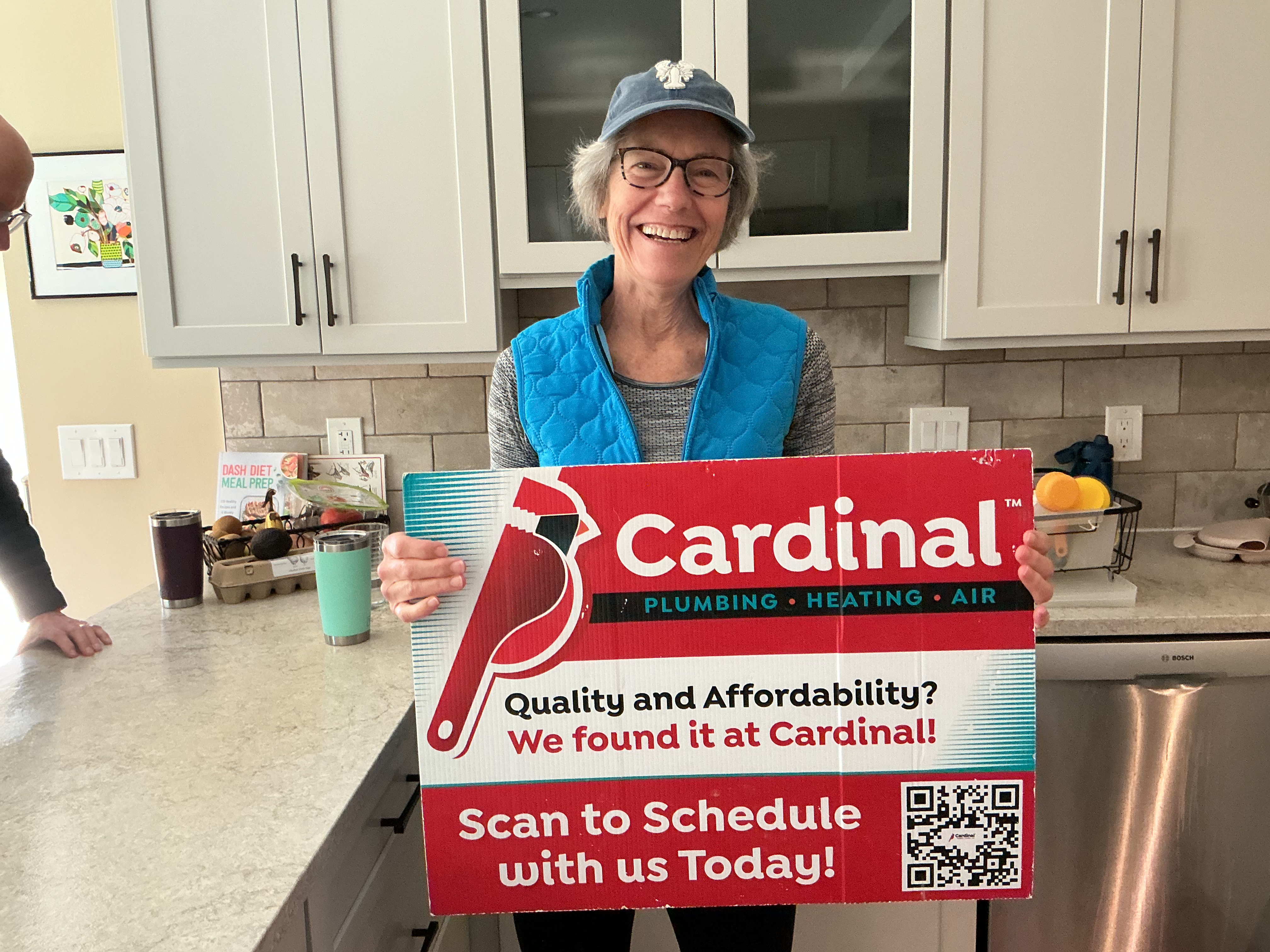 A satisfied homeowner beams while holding a Cardinal Plumbing Heating & Air Inc sign, showcasing trust and friendly service.