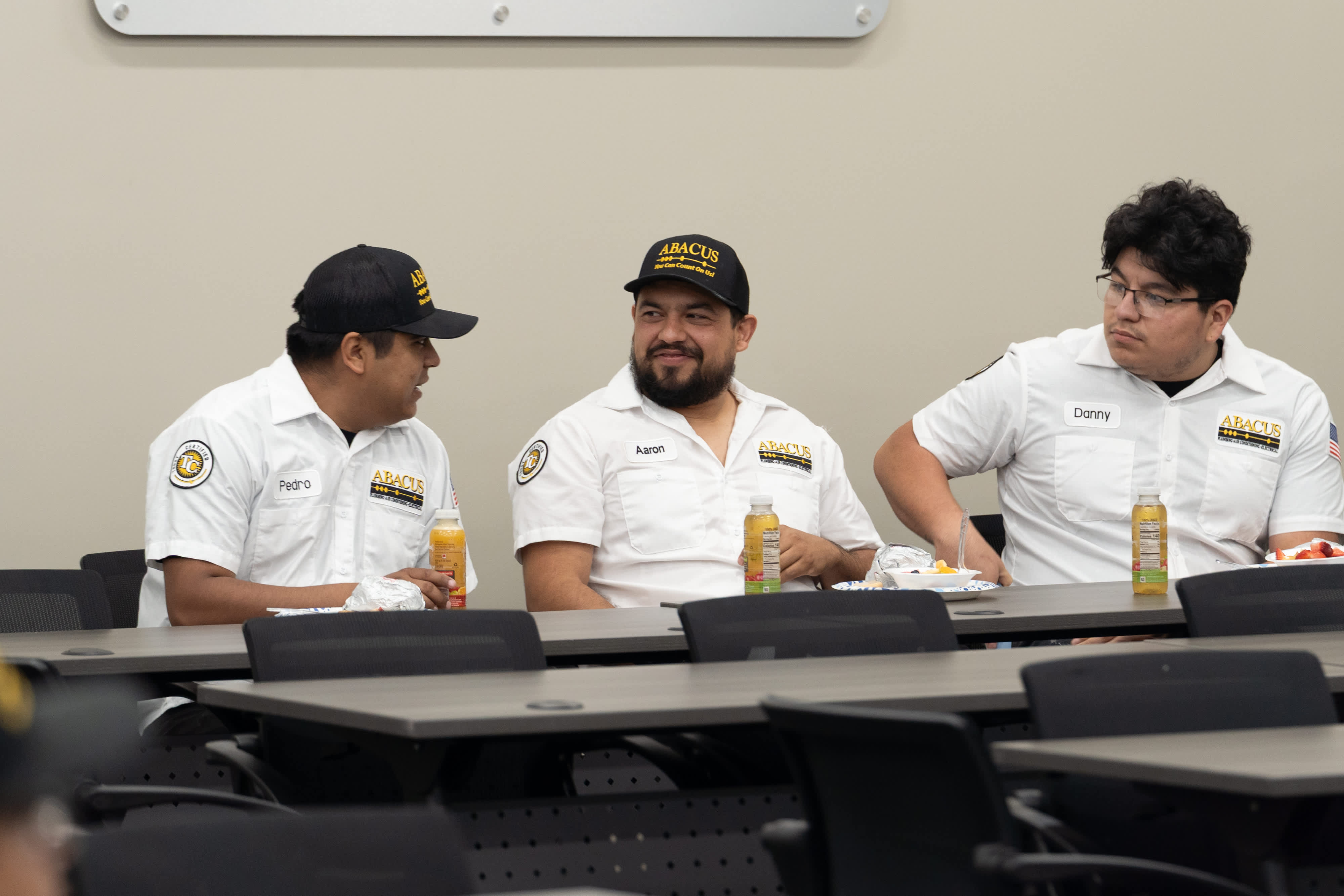 Friendly technicians from Abacus Plumbing, Air Conditioning, & Electrical showcase a professional, approachable team atmosphere during staff training and lunch.