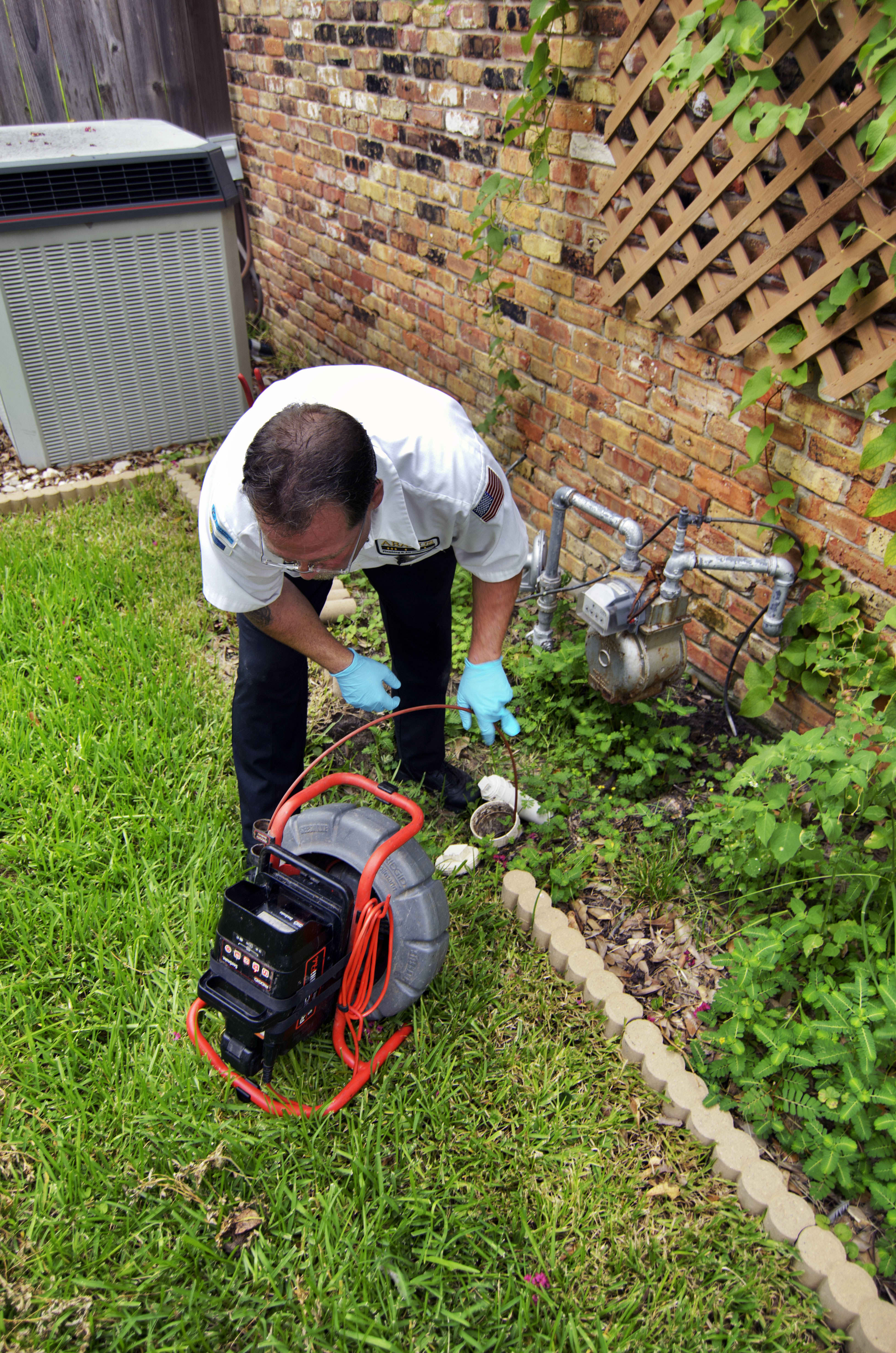 A uniformed technician from Abacus Plumbing, Air Conditioning, & Electrical confidently clears a stubborn outdoor drain, showing careful, reliable workmanship.