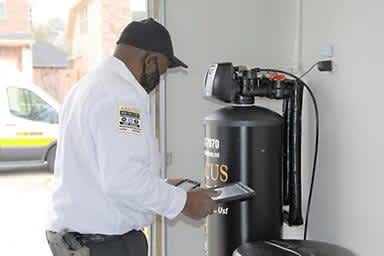 A skilled technician from Abacus Plumbing, Air Conditioning & Electrical demonstrates careful, modern service while inspecting a home's water treatment system.