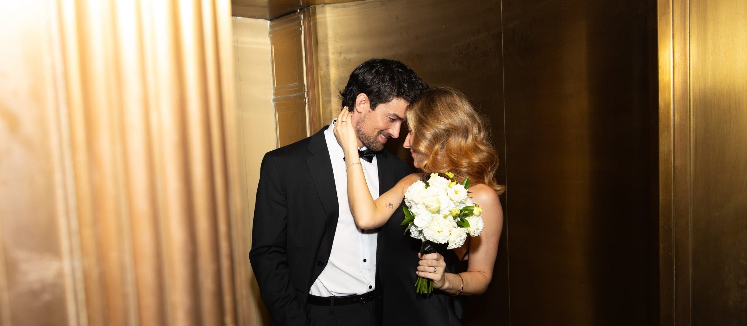 Ben and Joana embracing in a golden elevator on their wedding day in New York