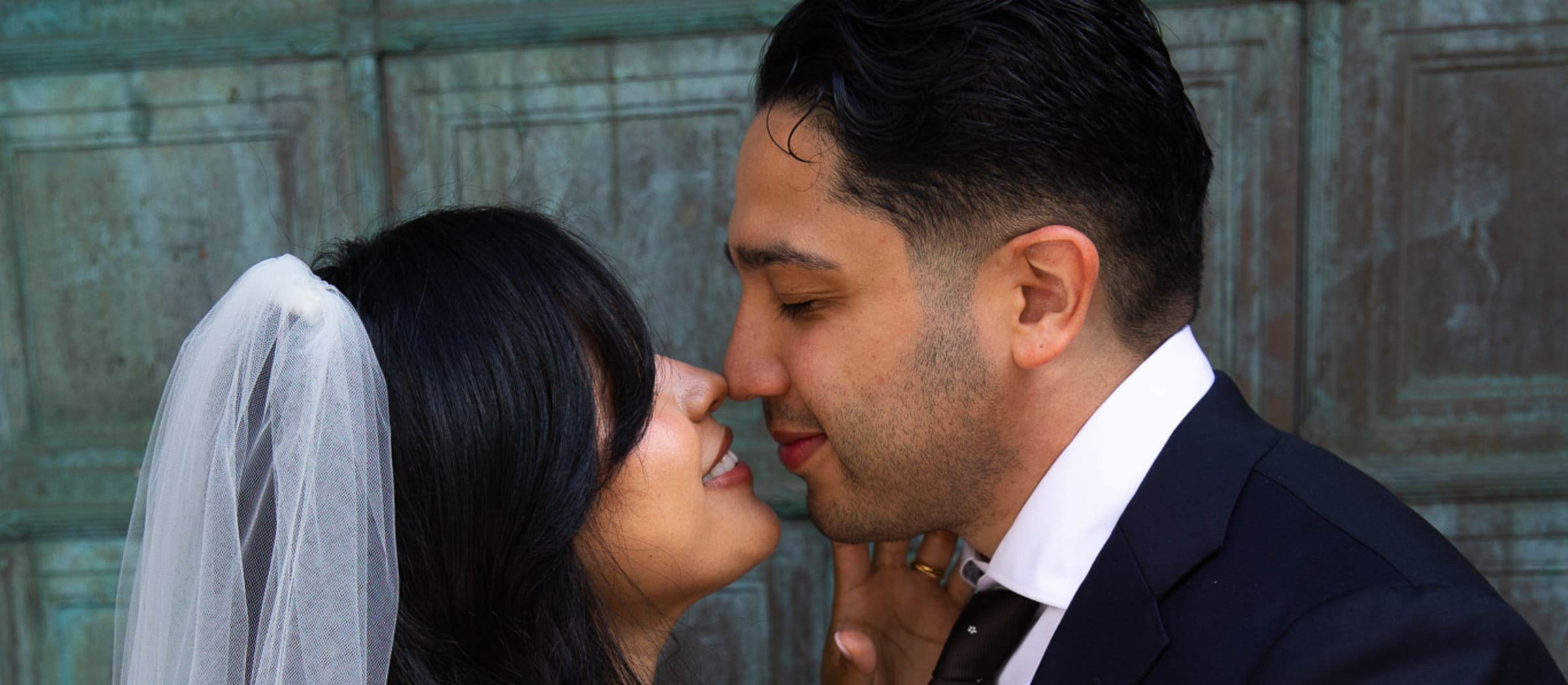 Patricia and Carlos kissing outside the bronze doors of city hall after their wedding