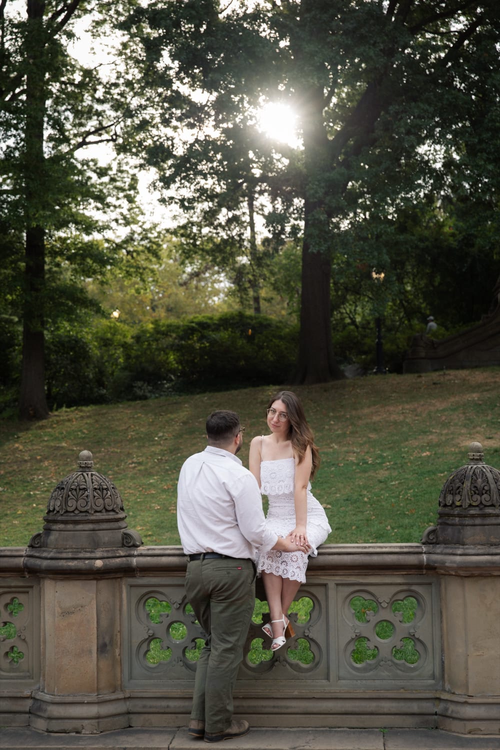 Sydney sitting on a stone balustrade with Braden leaning in beside her, sun through the trees