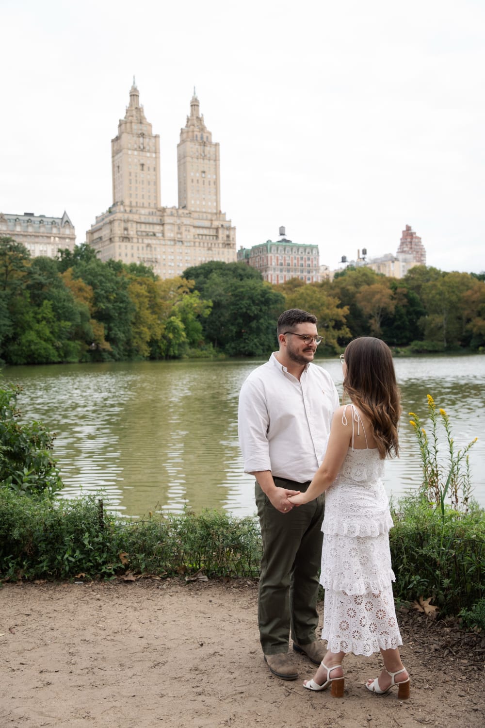 The engaged couple facing each other at the edge of the Lake, the San Remo on the skyline