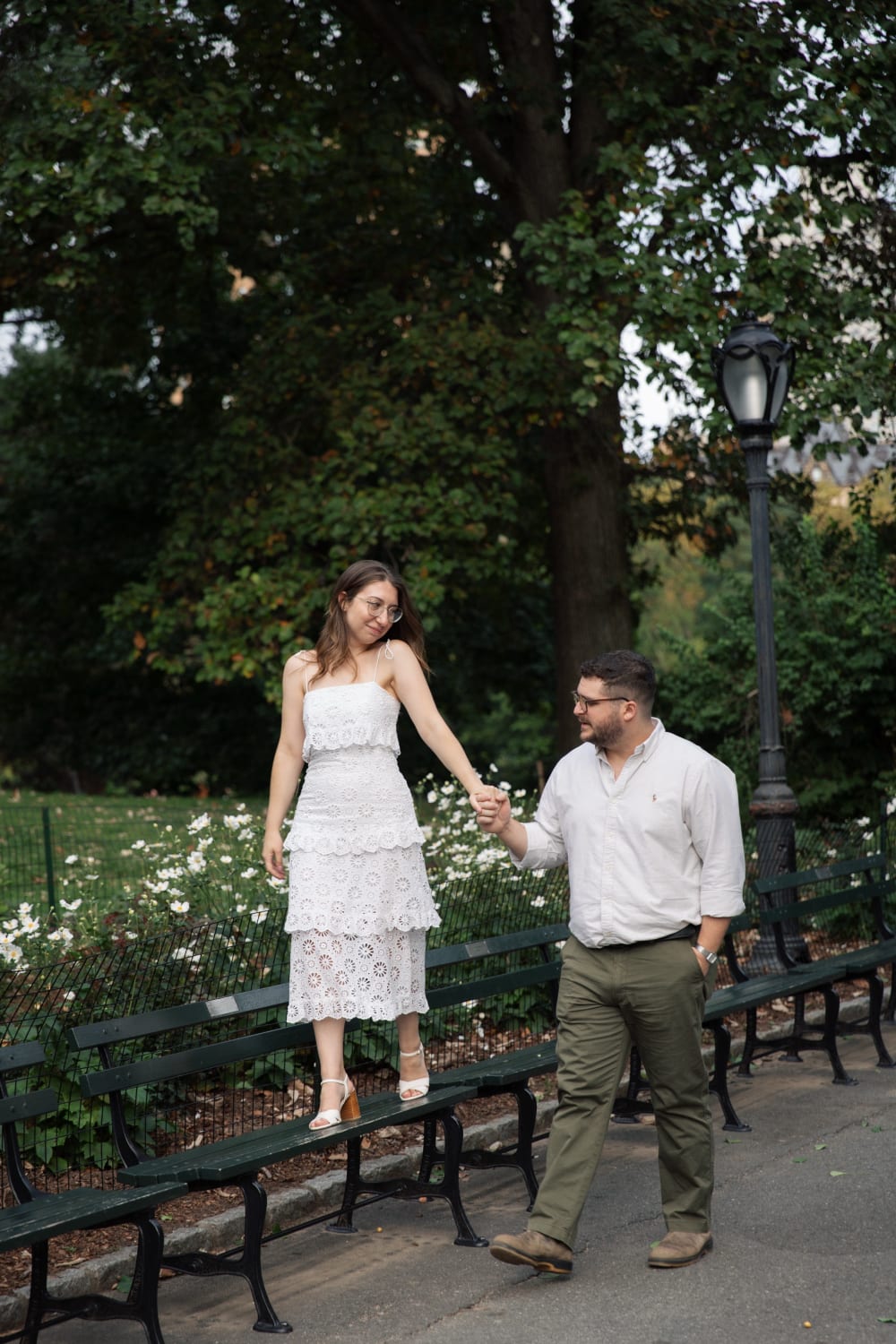 Sydney standing on a park bench holding Braden's hand beside a flower bed
