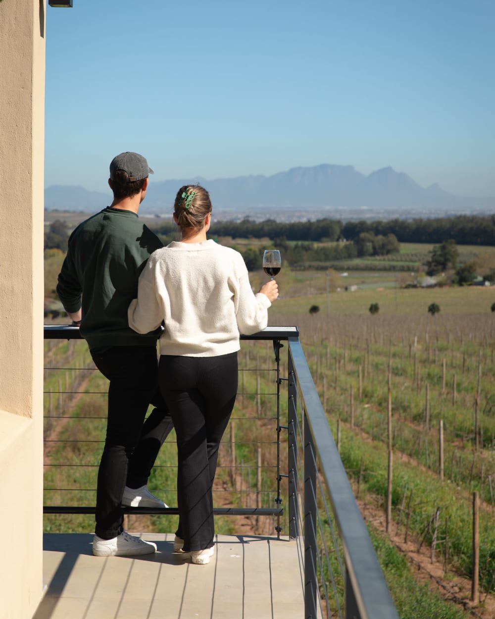 A couple with wine glasses on a balcony looking out over the Grangehurst vineyards