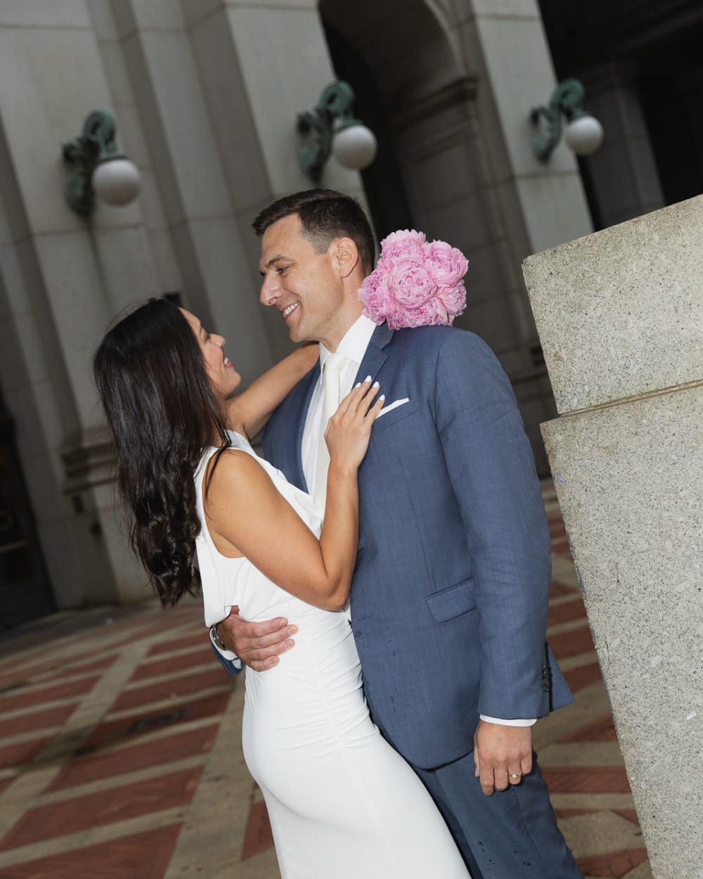 Bride reaching up to her groom beside the stone columns of a building near City Hall, Manhattan