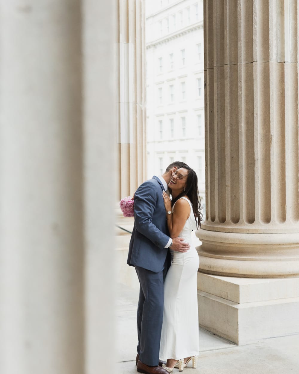 Newlyweds holding each other between two tall stone columns in Lower Manhattan