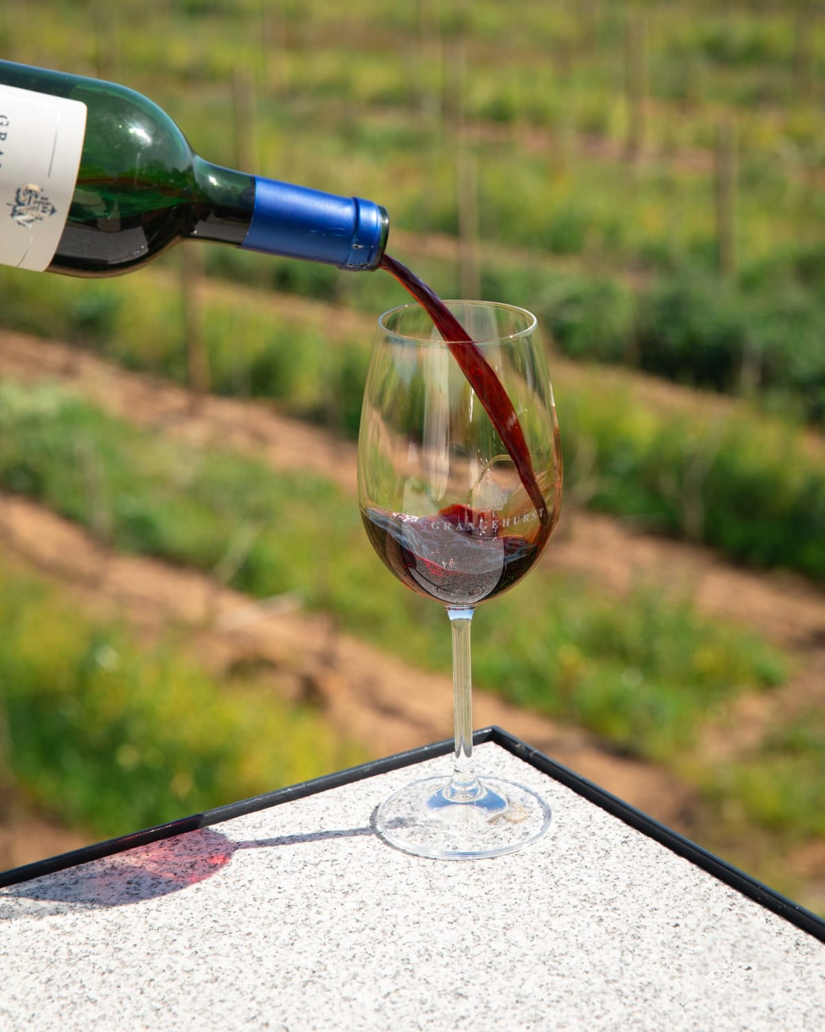 Red wine being poured into a glass above the vineyard rows at Grangehurst