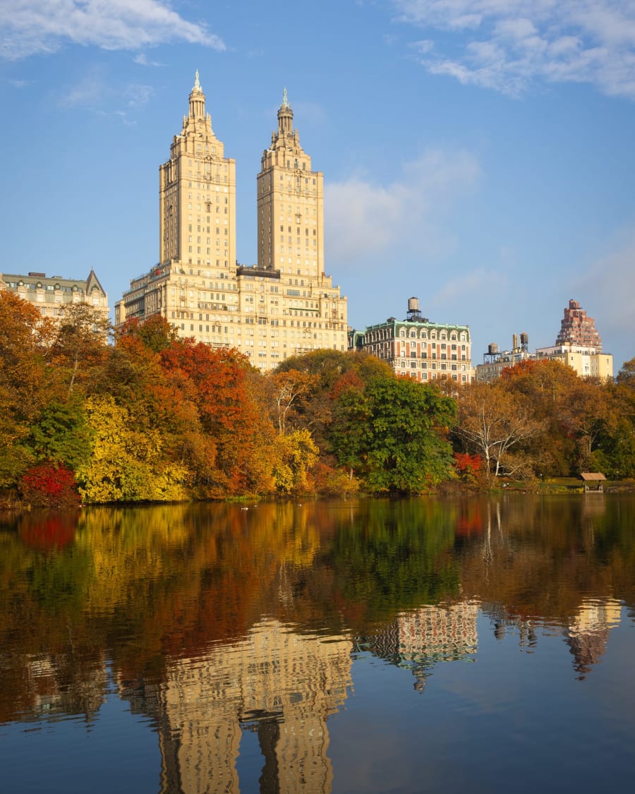 The San Remo towers above the Lake in Central Park, with orange and red trees reflected in the water