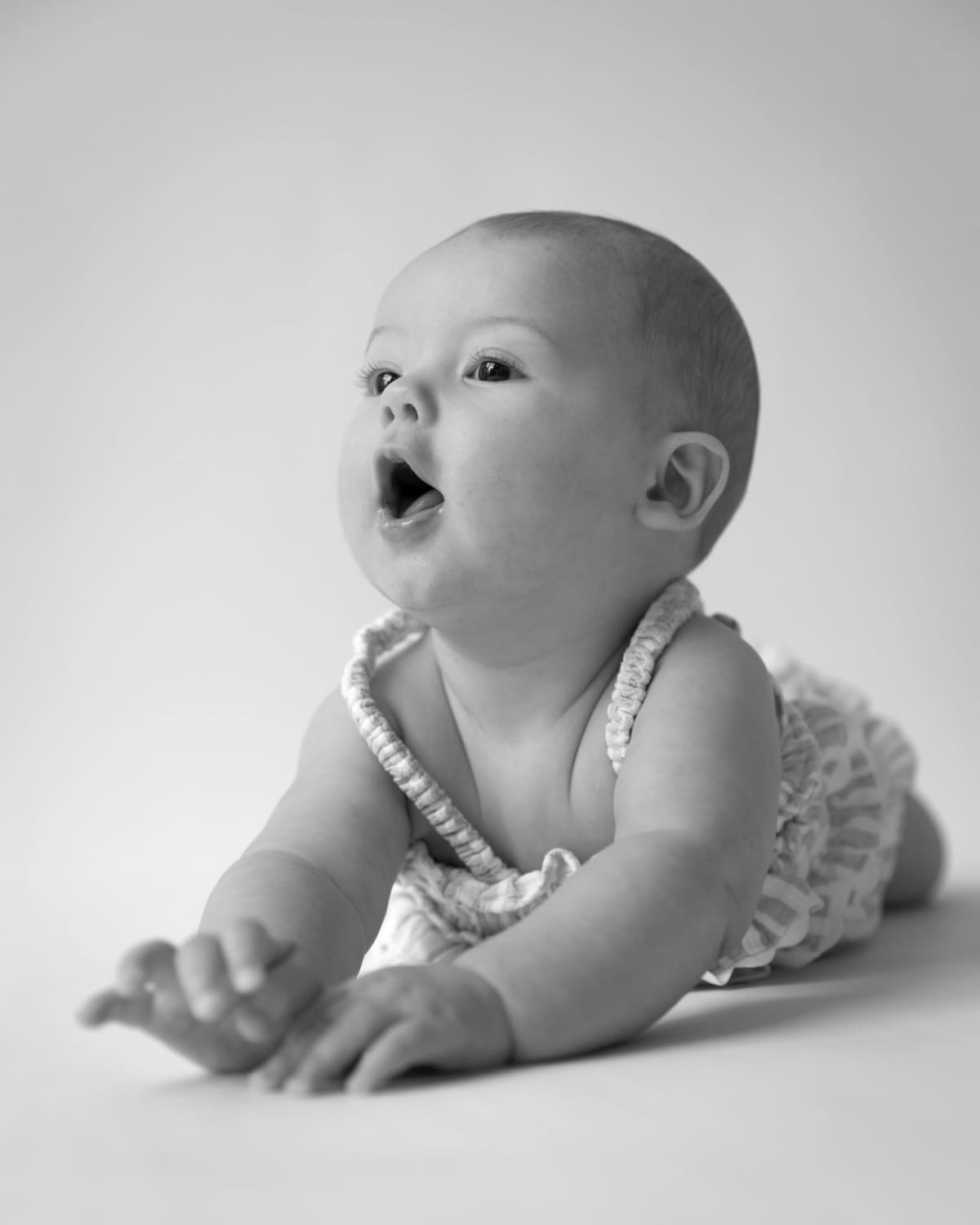 A baby lying on her tummy, looking up with her mouth open in delight