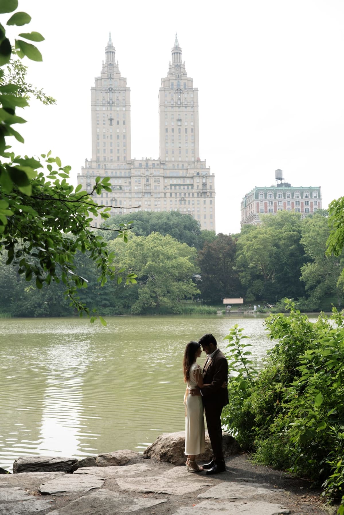 A couple kissing by the lake in Central Park with the San Remo towers behind