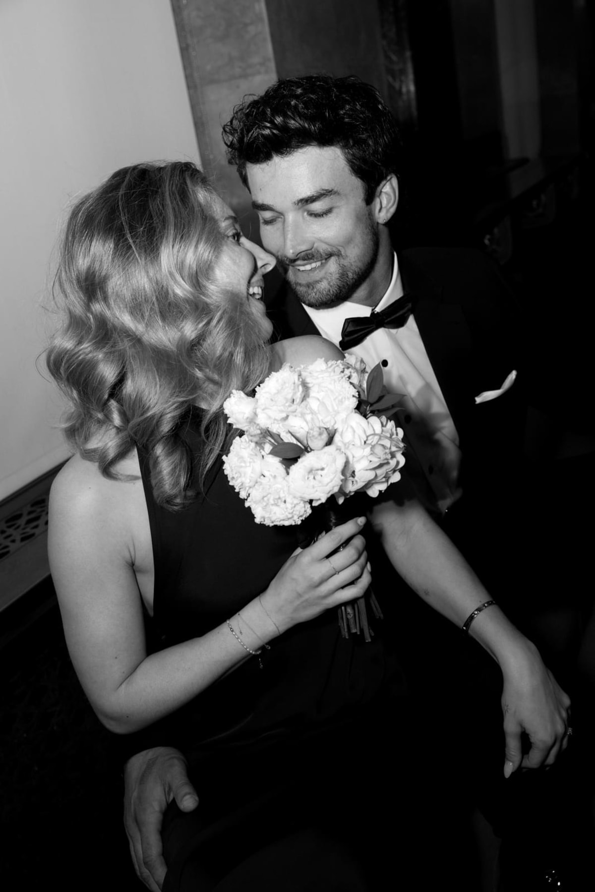 A bride and groom laughing together, holding a white bouquet