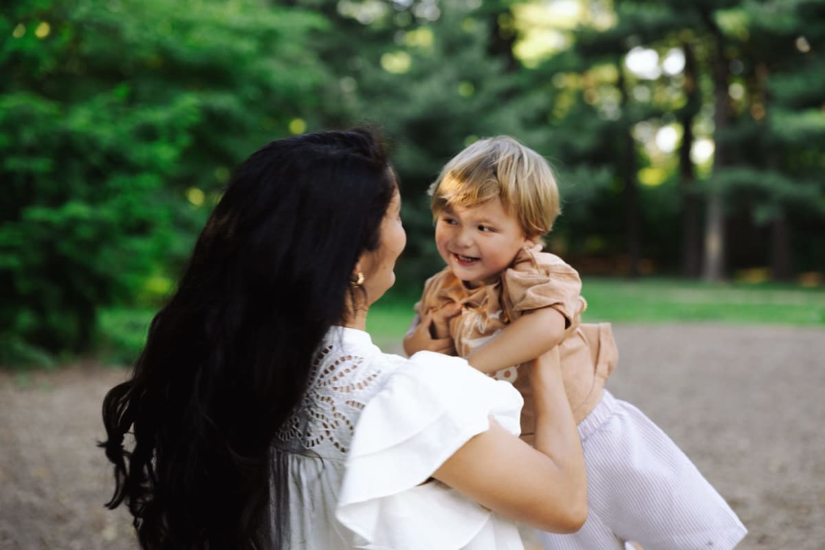 A mother lifting her laughing toddler among the trees