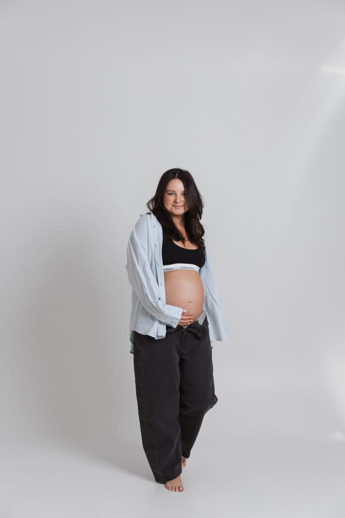 An expecting mother standing against a pale studio backdrop