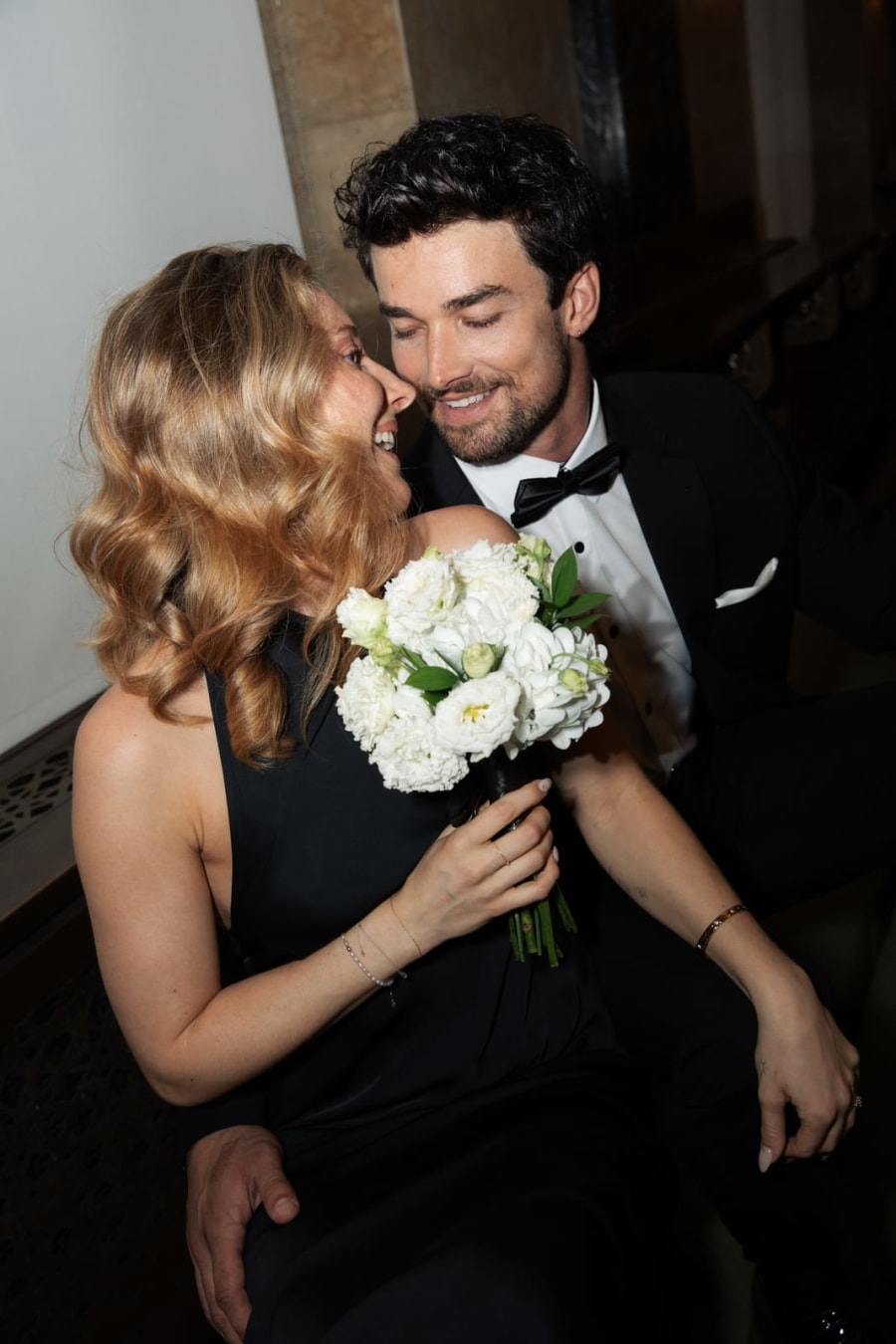 A bride and groom laughing together inside the City Clerk's office, holding a white bouquet