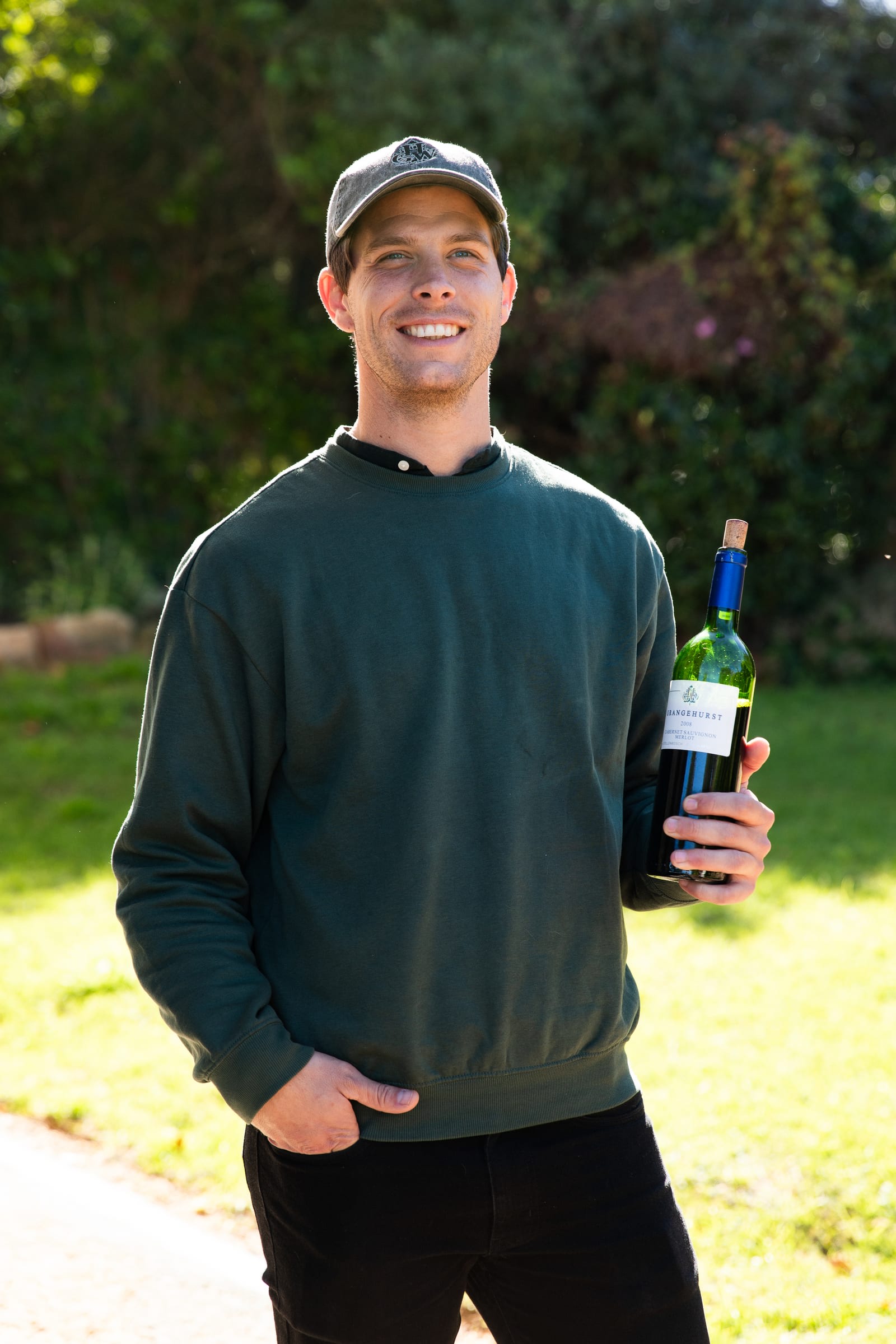 A smiling man holding a bottle of Grangehurst wine at a boutique winery in Stellenbosch, South Africa