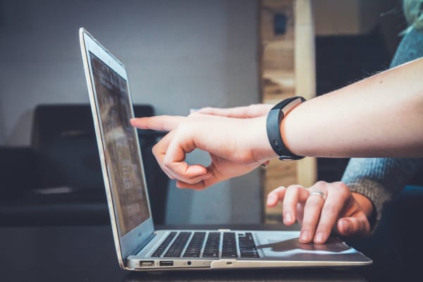 Photo of two people pointing at a laptop on a wodden desk