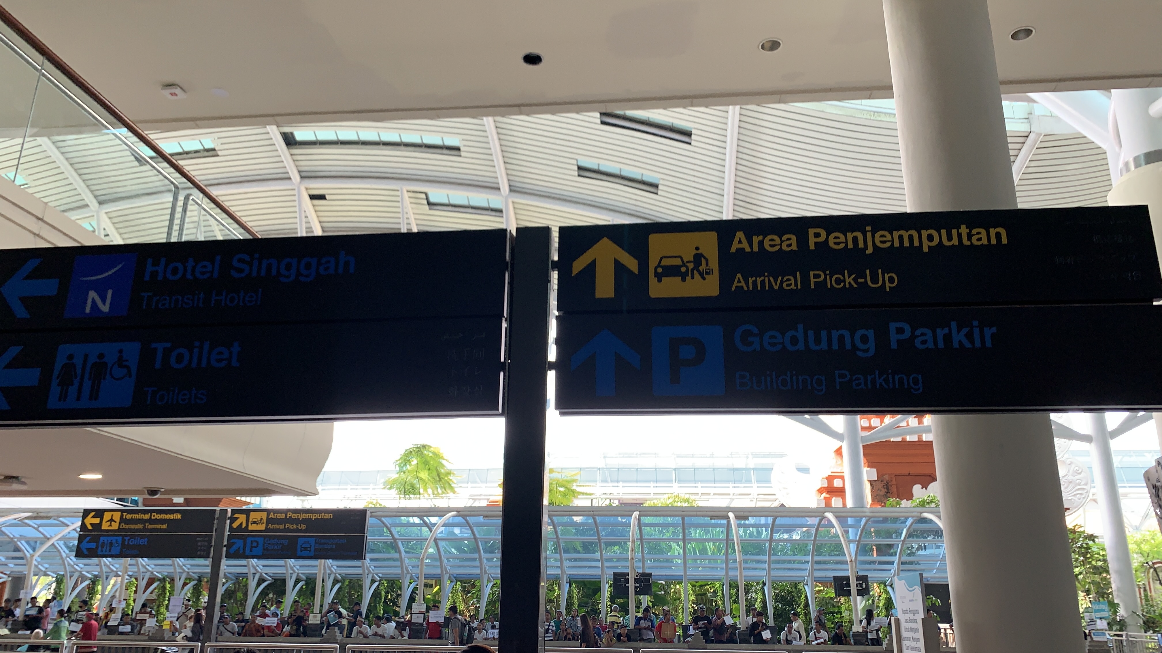 Airport signs directing to Arrival Pick-Up, Building Parking, Transit Hotel, and Toilets at Bali's Ngurah Rai International Airport