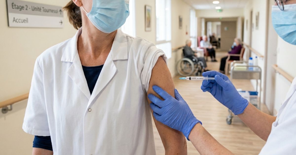 Seringue de vaccin antigrippal et blouse de soignant dans un couloir d'Ehpad, ambiance sobre