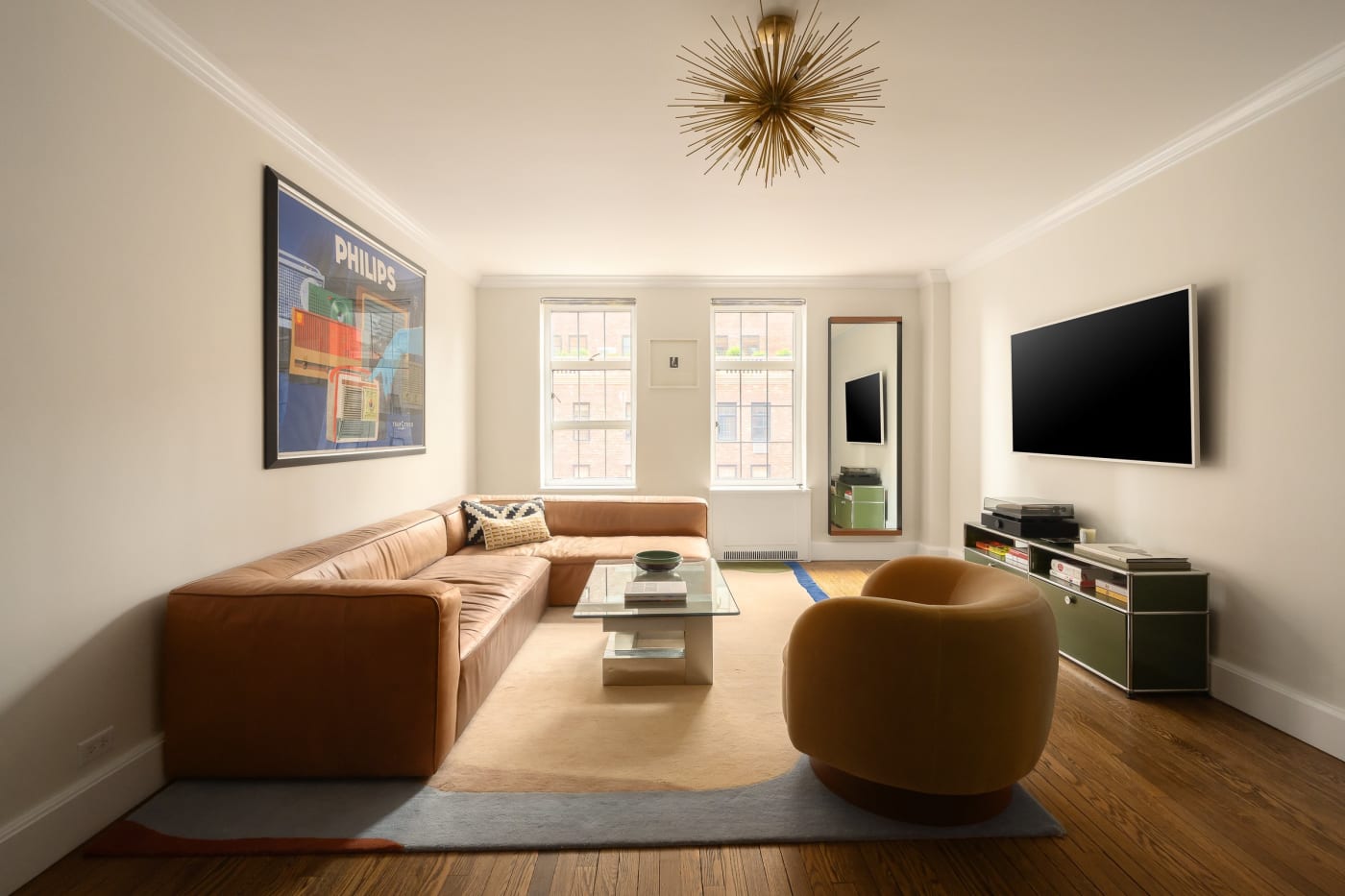 The living area of Residence 16J: leather sofa, swivel chair, and gallery wall under a sunburst pendant