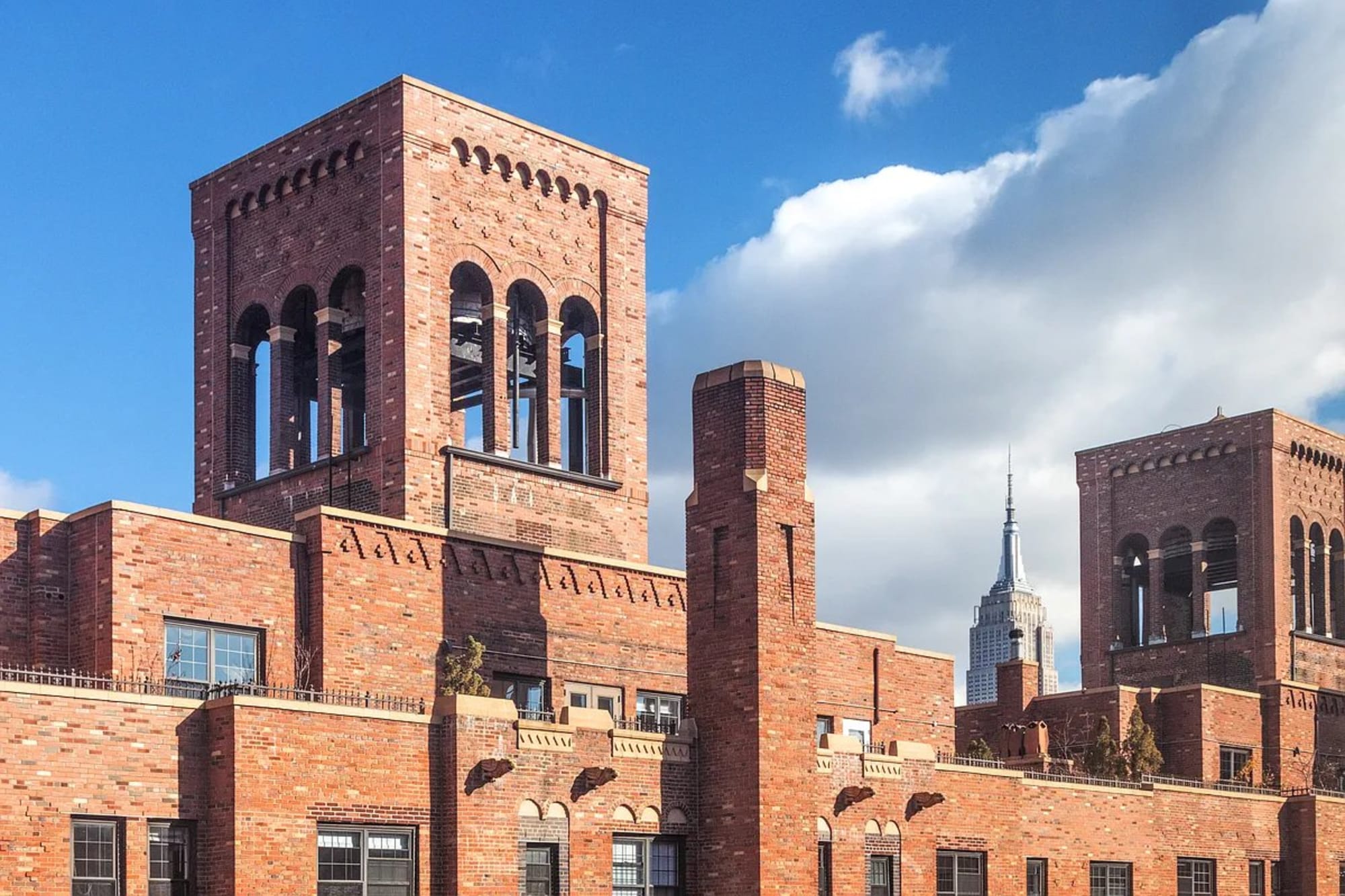 The brick tower crowns of London Terrace against a blue sky, the Empire State Building rising beyond