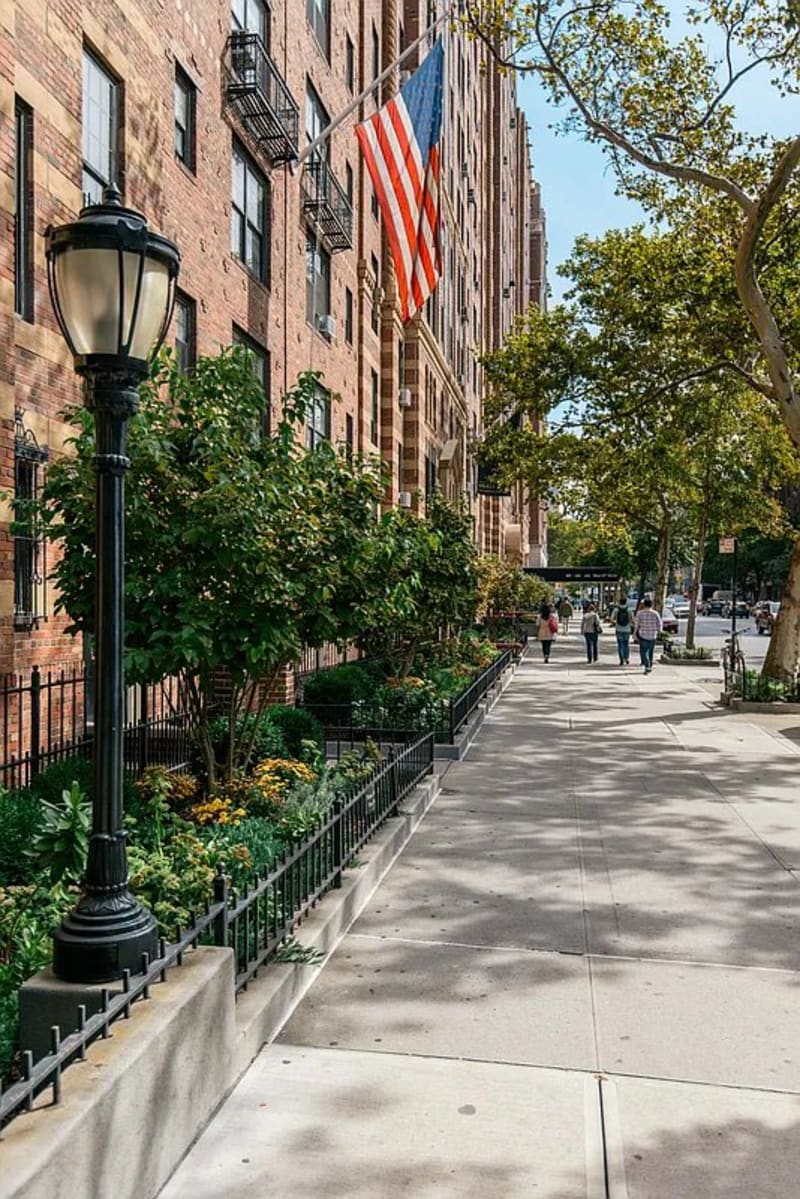The tree-lined sidewalk along London Terrace on West 24th Street, an American flag over the entrance