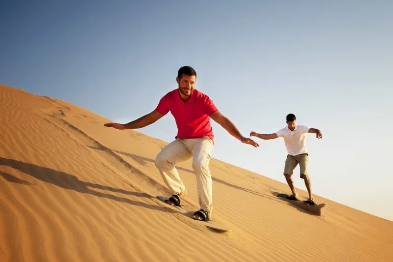 Tourist sandboarding down golden dune during morning safari Abu Dhabi