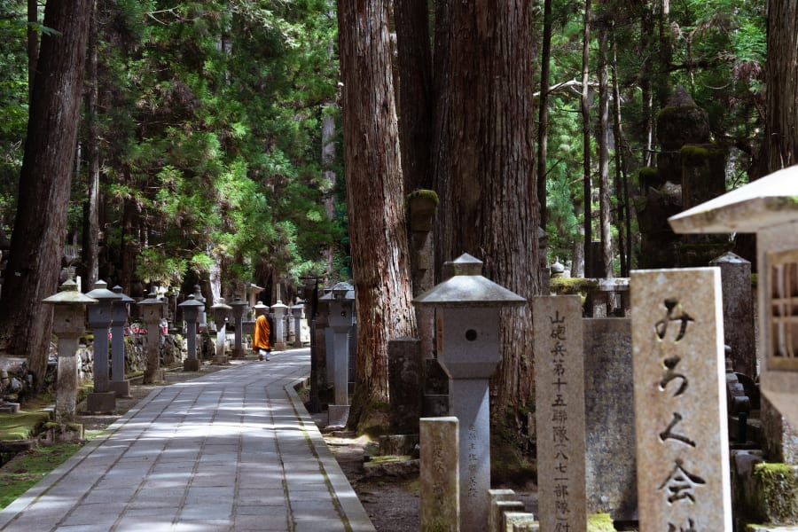 L’allée pavée d’Okunoin s’enfonce sous les cèdres, entre les stèles et les lanternes de pierre ; au loin, un moine en robe safran