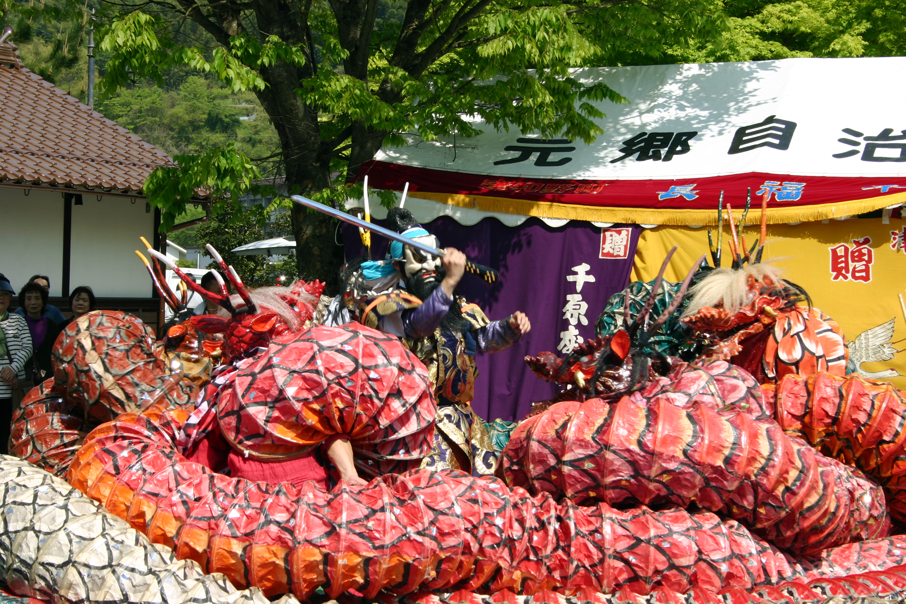 Un danseur masqué, sabre levé, face aux anneaux du grand serpent de l’Iwami kagura