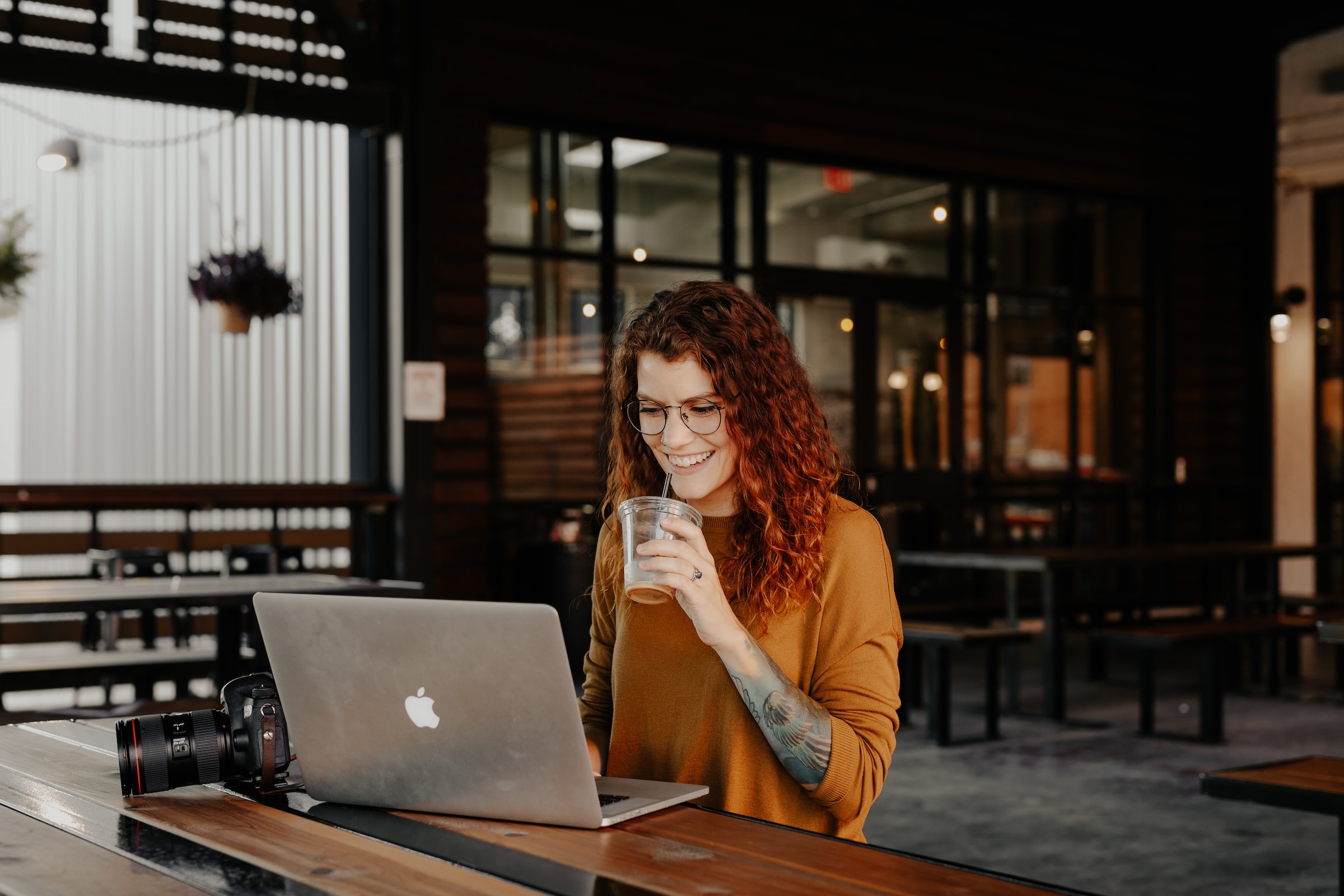 digital creator woman in brown long sleeve shirt sitting by the table using macbook