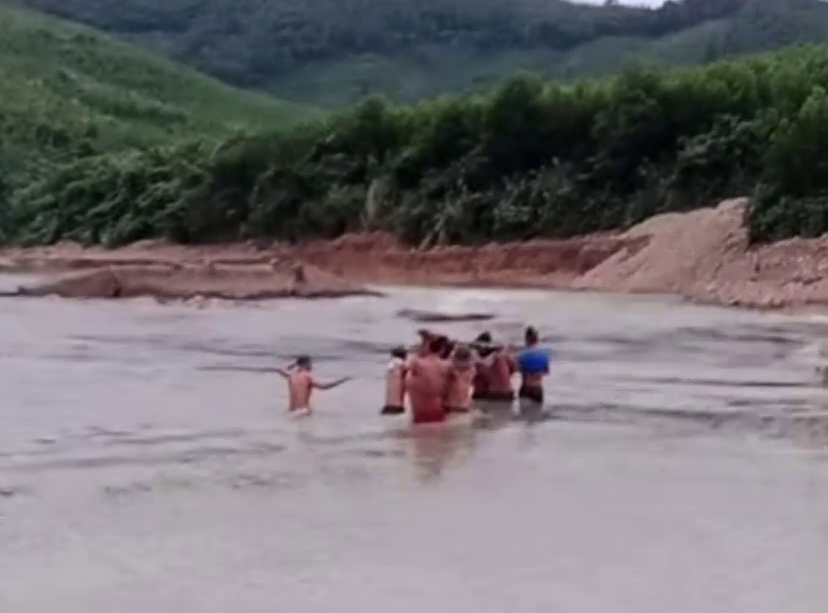 Hàng chục thanh niên thôn Cát thay nhau gánh sản phụ trên võng vượt suối và ngầm nước lũ chảy xiết để đến bệnh viện cấp cứu - Ảnh: cắt từ clip