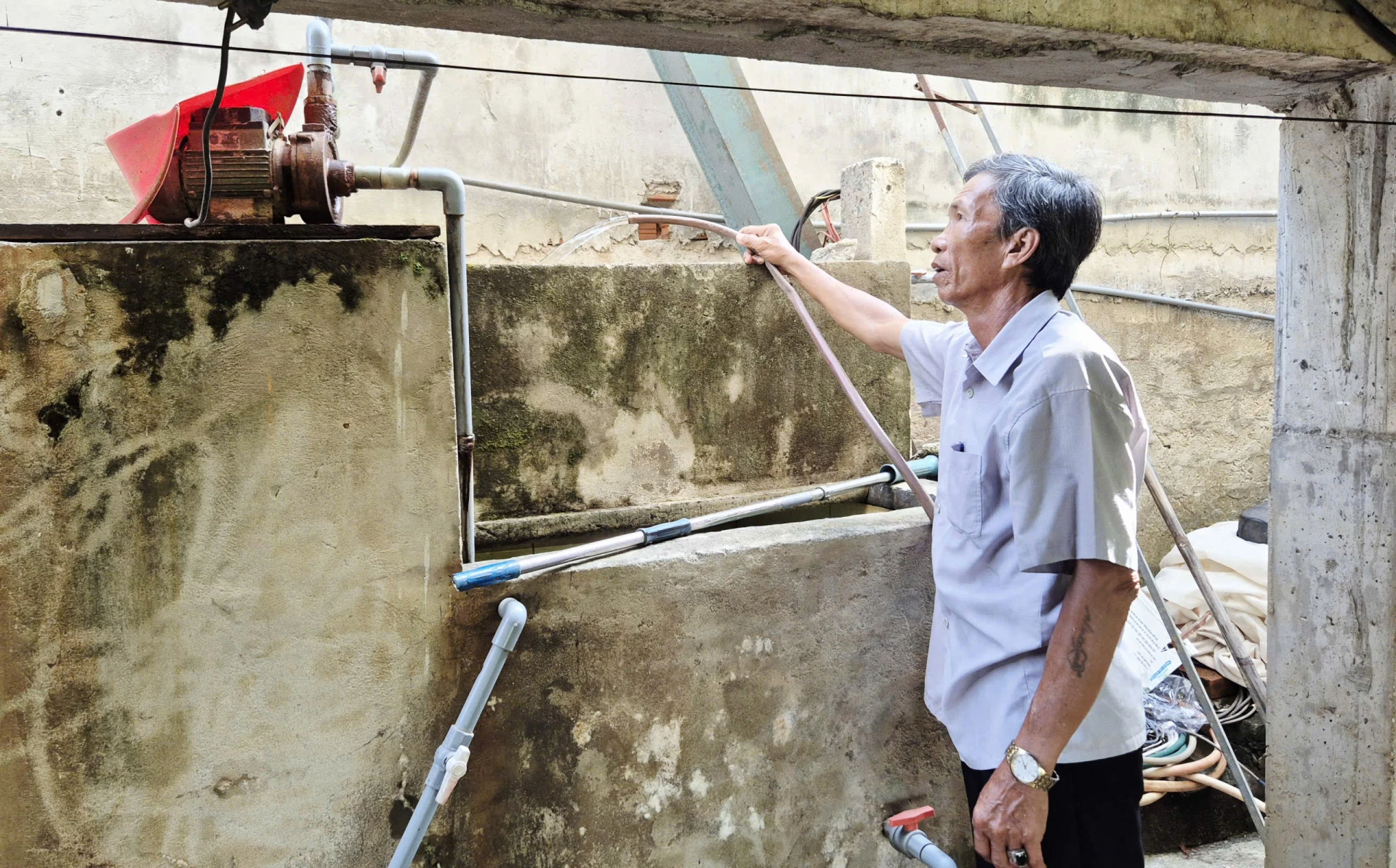 Ông Bùi Khảm bên hệ thống bể lọc thủ công do gia đình đầu tư để xử lý tạm thời nguồn nước nhiễm phèn phục vụ sinh hoạt - Ảnh: K.S