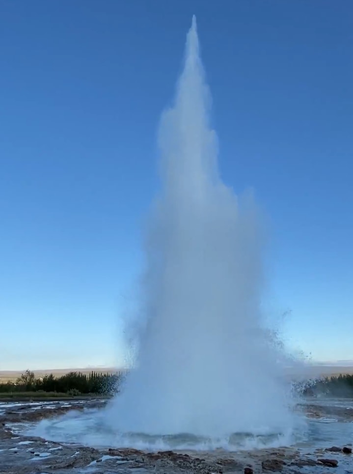 Strokkur geyser erupting at sunset with golden mist