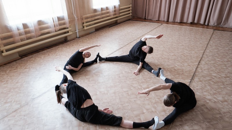 Vier junge, bewegliche Tänzer in Sportkleidung sitzen mit ausgestreckten Beinen auf dem Boden eines modernen Tanzstudios