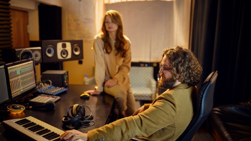Männlicher Musikproduzent und Sängerin in einem Tonstudio mit Synthesizer und Mischpult am Arbeitsplatz