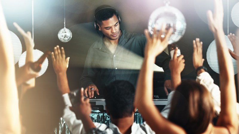 Feiernde Menschen auf einer Tanzfläche bei einem DJ-Event mit erhobenen Händen und Lichteffekten